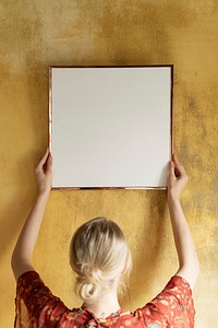 Woman hanging a frame on a grunge yellow wall