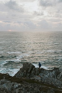 Man standing on the rocks by the beach at sunset
