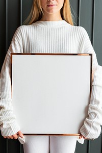 Woman in a white sweater holding a wooden frame