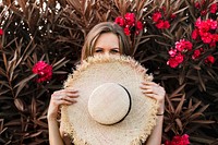 Woman holding a straw hat in front of a shrub