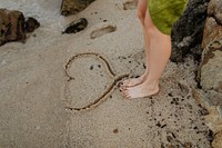 Woman standing by a drawing heart on the beach