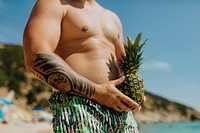 Tattooed man holding a pineapple at the beach