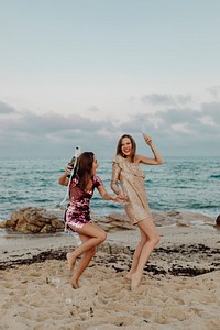Women dancing with glasses of champagne at the beach