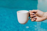 Woman holding a white coffee cup by the pool