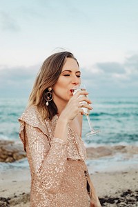 Woman in a gold dress having a glass of champagne at the beach