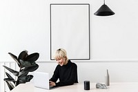 Woman working on her laptop with a blank frame hanging on a wall