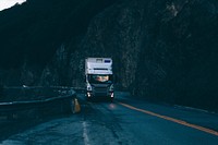 A silver Scania truck driving down an empty road in the mountains in the evening. Original public domain image from Wikimedia Commons