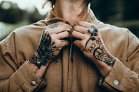 Tattooed man buttoning  brown shirt closeup