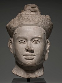 Head from an image of a diefied king carved in sandstone wearing a very elaborate crown and a diadem tied with a knot at the back of his head. Crisply delineated facial features carved in high and low relief. Original encrusted patina. First Angkor style, style of Koh Ker, Cambodia.. Original from the Minneapolis Institute of Art.