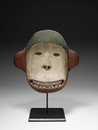 rounded, concave face; rounded ears on sides of head; wide, open, ovoid mouth with eight peg teeth; small eyes; rather flat nose with triangular nostrils; top of head is green; face is white; mouth, chin and ears are rust red. Original from the Minneapolis Institute of Art.