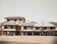 view across a wide street to a building with people standing on balconies, seated in rickshaws, standing on street in front of porches; man standing on blue tile roof at center. Original from the Minneapolis Institute of Art.