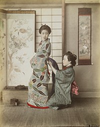 Two young women wearing traditional Japanese garments; kneeling woman at right wearing blue and grey striped kimono assists standing woman at left, wearing a flowered kimono with blue ground, with tying her obi; folding screen and hanging scroll in background. Original from the Minneapolis Institute of Art.