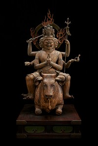 Figure with six heads, arms, and legs astride crouched bull on wood base; metal bands around wrists, some biceps, and most ankles; halo with flames attached at back; two hands of two arms together in praying position, other arms bent and flare outwards. Upper left arm holds long staff, lower one holds implement with "curly q"-shaped end. Upper right arm holds a trident. Lower right arm fingersshaped like it was holding something in hand. Three bottom heads have crystal inlay eyes. Three smaller heads on top considerably smaller. Original from the Minneapolis Institute of Art.