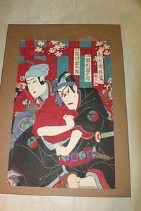 Center/right print; two actors in center of image; actor in front wears heavy red eye makeup, black robe with red underneath, a red obi with sword tucked in, and a blue sash around his head; actor in back wears red and blue robe with light blue headdress; print is richly colored with red, black, blue, and teal; white blossoms in background, text in cartouches in URQ. Original from the Minneapolis Institute of Art.