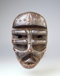 Heavy forehead; vertical rib down center of face with 3 pairs of horizontal ribs (bottom pair unattached at sides); tacks on forehead, lips and across ribs. Original from the Minneapolis Institute of Art.