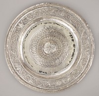 large, thin, round silver platter; central three-dimensional applied large flower form with five petals and cluster of six round elements at center; three round patterned bands around central flower (from interior outward): zigzagging ribbon around central circle, row of feathers or leaves, intertwined football shapes on stippled ground; outer rim has wide band of scrolls, flowers and foliage; outer raised band with looped motif around a round core. Original from the Minneapolis Institute of Art.