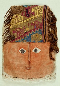 square-shaped face made of stuffed cloth; woven multi-colored headband with geometric shapes and hairlike brown fringe; face painted orange with small red smiling mouth; disk-shaped wood irises and wedge-shaped protruding nose; mounted inside a plexi case. Original from the Minneapolis Institute of Art.