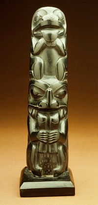 Small totem of carved slate ? with carefully finished surface. The upper animal is a bear squatting with his fore-paws under his chin; he is identified by his protruding tongue, large round nose and sudden turn from nose to fore-head; his ears are missing. The lower animal seems also to be a bear, squatting with his tail turned up in front behind his hind legs. He is swallowing some being the legs and hands of which hang out of this mouth; he is grasping the lower legs with his fore-paws. The difference between this bear and the upper one is due to the fact that his forehead is farther foward so that the other bear can perch on his head. This necessitates the spine in the middle of his nose to indicate the sharp turn from nose to forehead. late 19th century.. Original from the Minneapolis Institute of Art.