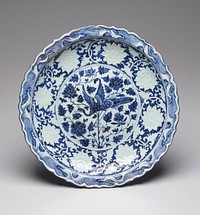 Blue-and-White dish, porcelain; decorated in a deep blue in the center with a large peahen flying amongst peonies, the cavetto molded with a band of peonies in white in a blue ground, the rim with a border of stylized waves and a molded foliated edge; the reverse has a typical wide unglazed base with a short foot ring and the exterior is decorated with a band of scrolling lotus. Original from the Minneapolis Institute of Art.