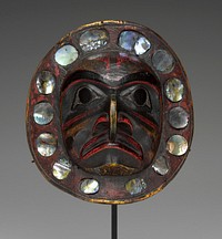 convex circular form, carved in high relief with a mask bearing a combination of human and hawk attributes; painted with red, yellow, green and black pigments; encircled by 14 abalone shell plaquettes in round and oval shapes. Original from the Minneapolis Institute of Art.