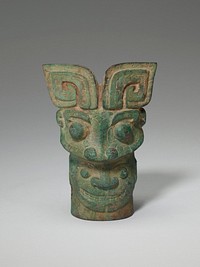 An eccentric combination of four masks occurs on this bronze. A forceful t'ao-t'ieh head with recumbent C-shaped horns, the borders decorated with straight and T-shaped scores, appears on one side of the top. This monster bites on a human head with the broad nose typical of many early masks. On the other side a ram's head, with horns turned down, bites on a head resembling a t'ao-t'ieh but with a raised elephant's trunk instead of the usual ridge in the central line. This remarkable and unusual piece is a powerful example of early Chinese sculpture. Patina green.. Original from the Minneapolis Institute of Art.