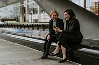 Businesswomen holding smartphone, laughing together