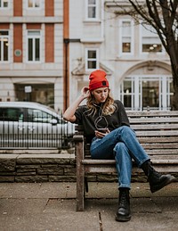 Blonde woman listening to music, sitting on a bench