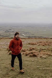 Man wearing orange puffer jacket, walking on hill