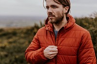 Man wearing orange puffer jacket, walking on hill