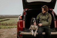 Man sitting in car trunk with dog