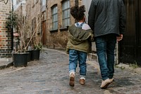 Little girl holding father's hand, walking in city