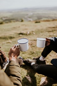 Campers holding mugs, sitting on grass field