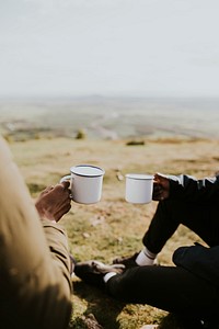 Campers holding mugs, sitting on grass field