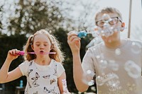 Happy siblings blowing bubbles,  playing in the backyard