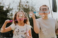 Happy siblings blowing bubbles,  playing in the backyard