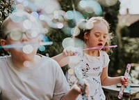 Happy siblings blowing bubbles,  playing in the backyard