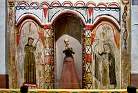                         Detail of one of several elegant, hand-painted reredos (altar screens) and other intricate decorations that line the sanctuary walls of the El Santuario de Chimayo, a humble chapel in Chimayo, a New Mexico village on the "High Road," a winding route through the Sangre de Cristo mountains to and from the capital city of Santa Fe and the art and shopping mecca of Taos                        