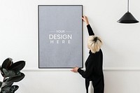 Blond haired Asian woman hanging a frame mockup on a white wall