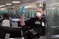 An officer with U.S. Customs and Border Protection Office of Field Operations gestures for arriving international travelers to proceed forward through the line at Dulles International Airport in Dulles, Va., March 18, 2020.