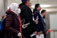 International travelers, some wearing protective masks and gloves, wait in line before meeting with U.S. Customs and Border Protection Office of Field Operations officers to review their travel documents as they arrive at Dulles International Airport in Dulles, Va., March 18, 2020.