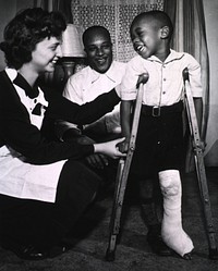 Public Health nurse assists in the healing process. A young boy, on crutches, his left leg in a cast, takes first steps with the aid of a Public Health nurse. Original public domain image from Flickr