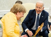 President Joe Biden shows a photo to German Chancellor Angela Merkel on Thursday, July 15, 2021, in the Oval Office of the White House. (Official White House Photo by Adam Schultz). Original public domain image from Flickr