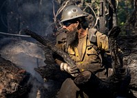 Cade Grismer, El Dorado Hot Shot, cuts trees during wet mop duties on the Caldor Fire, El Dorado National Forest, California. USDA Forest Service photo by Cecilio Ricardo. Original public domain image from Flickr