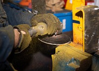 Aviation Support Equipment Technician paint off of a forklift part aboard the Expeditionary Sea Base. Original public domain image from Flickr