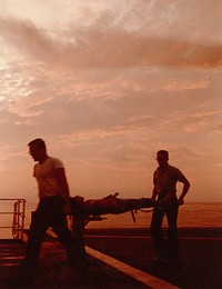 A wounded U.S. Marine is carried across the small flight deck of the hospital ship USS Repose (AH-16) after being transported by helicopter from Chu Lai, South Vietnam, in the early morning light. K-31167. April 23, 1966. Photo by J01 Jim Falk. 10/11/2022: Navy Medicine Historical Files - Subject - Vietnam War 