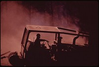 "Caterpillars" work in dust and soot hauling logs to landing area where they will be loaded onto trucks. Face mask filters ash and soot-filled air so driver can breathe, September 1973. Photographer: O'Rear, Charles. Original public domain image from Flickr