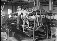 Many youngsters here. Some boys and girls were so small they had to climb up on to the spinning frame to mend broken threads and to put back the empty bobbins, January 1909. Photographer: Hine, Lewis. Original public domain image from Flickr