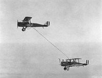 Capt. Lowell H. Smith and Lt. John P. Richter performing the first aerial refueling on 27 June 1923. The DH-4B biplane remained aloft over the skies of Rockwell Field in San Diego, California, for 37 hours. The airfield's logo is visible on the aircraft.