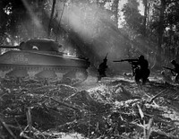 U.S. Army soldiers on Bougainville (one of the Solomon Islands) in World War II. Japanese forces tried infiltrating the U.S. lines at night; at dawn, the U.S. soldiers would clear them out. In this picture, infantrymen are advancing in the cover of an M4 Sherman tank.