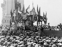 "Delivering the address - President's Day" depicts an address by United States President William McKinley at the Pan-American Exposition in Buffalo, New York on the day before his assassination. Crowd shot looking on the presidential gazebo. McKinley stands hatless, wearing a tuxedo, holding speech notes in his left hand.